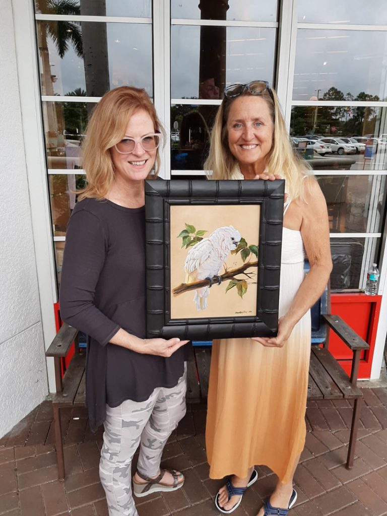 Martha Dodd on the right with Marti Koehler holding her newly purchased painting of a cockatoo.